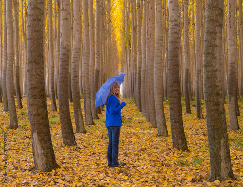 Woman in forest with blue umbrella and yellow fall colors