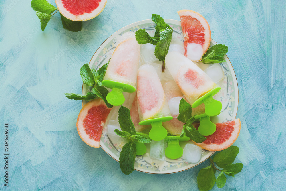 Homemade grapefruit popsicles with grapefruit slices on a mint wooden background. Top view. Copy space. Flat lay. Toned Homemade grapefruit popsicles with grapefruit slices on a mint wooden background. Top view. Copy space. Flat lay. Toned