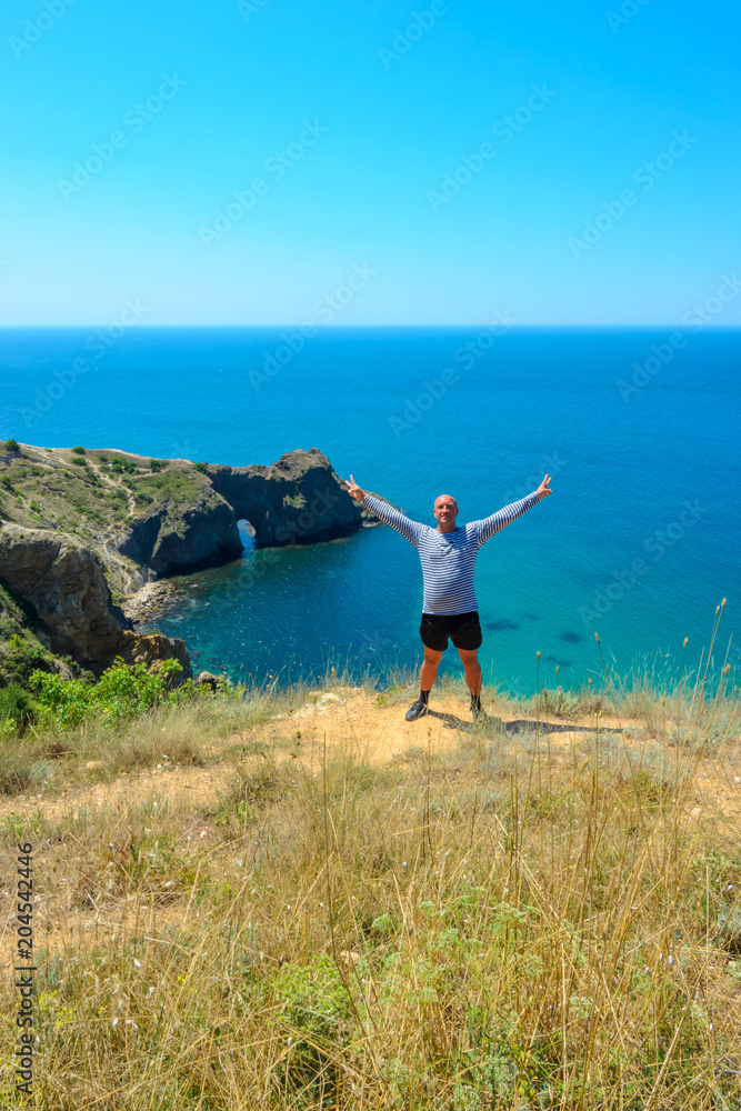 a positive person stands on the background of the sea on a cliff on a Sunny summer day a positive person stands on the background of the sea on a cliff on a Sunny summer day