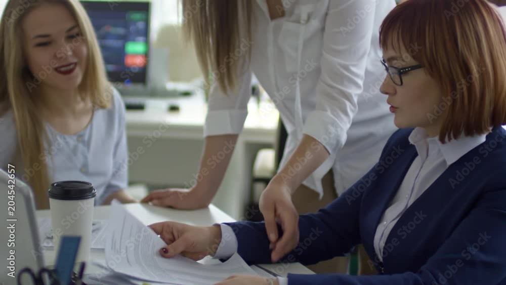 Tilt up of business lady sitting at office desk, sharing documents with female colleagues and explaining contract details Tilt up of business lady sitting at office desk, sharing documents with female colleagues and explaining contract details