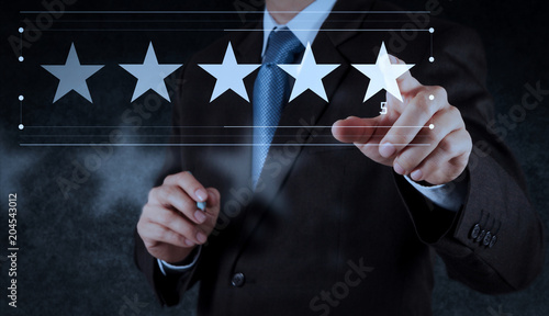 Five stars (5) rating with a businessman is touching virtual computer screen.For positive customer feedback and review with excellent performance. photo