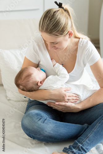 Beautiful young woman sitting on bed na drocking her sleeping baby boy