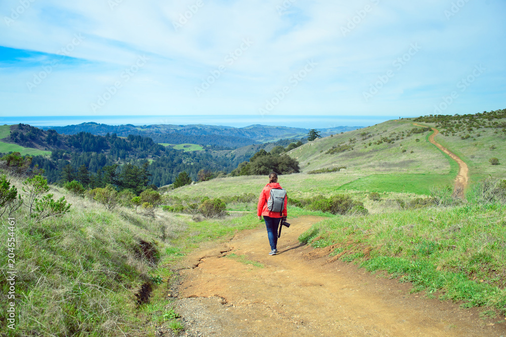 Hiker in red jacket with backpack on trail in beautiful landscape Hiker in red jacket with backpack on trail in beautiful landscape