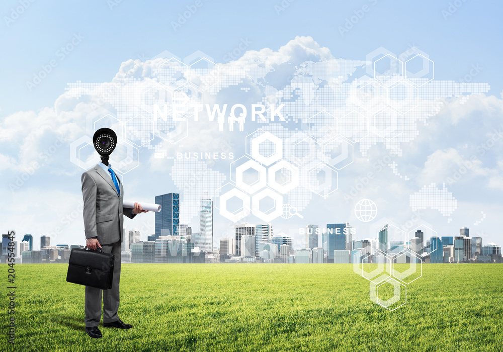 Camera headed man standing on green grass against modern cityscape Camera headed man standing on green grass against modern cityscape