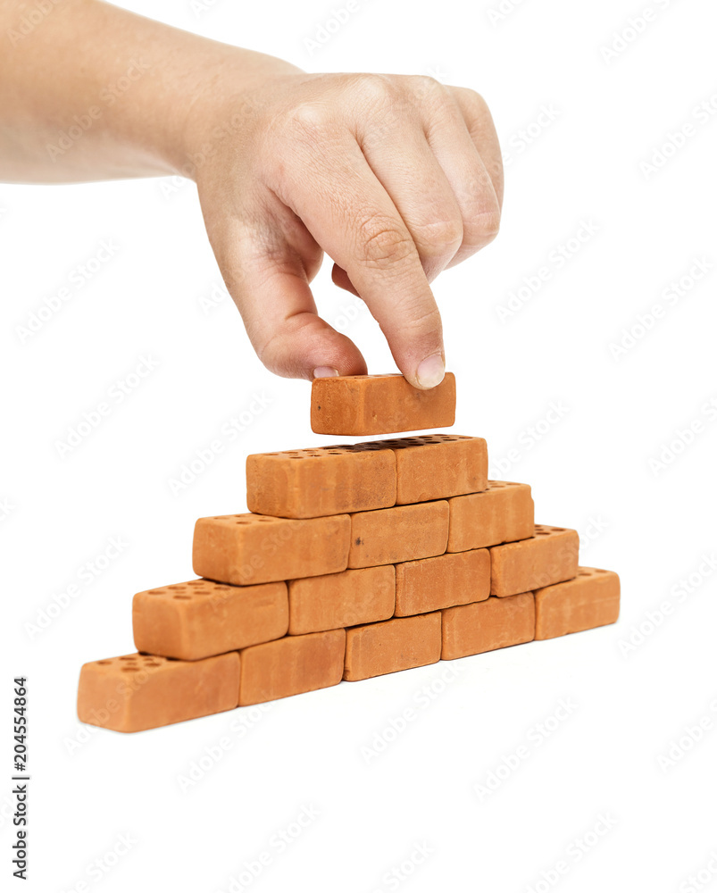 Concept of building and construction, a hand placing a brick on a wall, on a white background, including clipping path Concept of building and construction, a hand placing a brick on a wall, on a white background, including clipping path