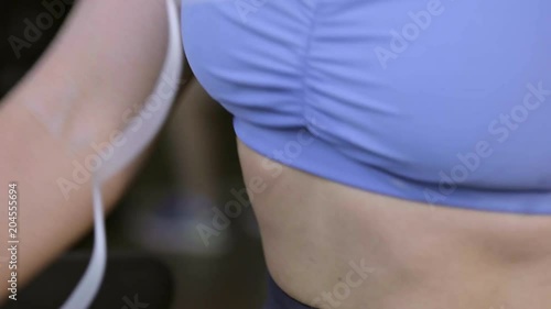 Tilt down shot of young woman doing brisk walk on treadmill and listening to music with headphones