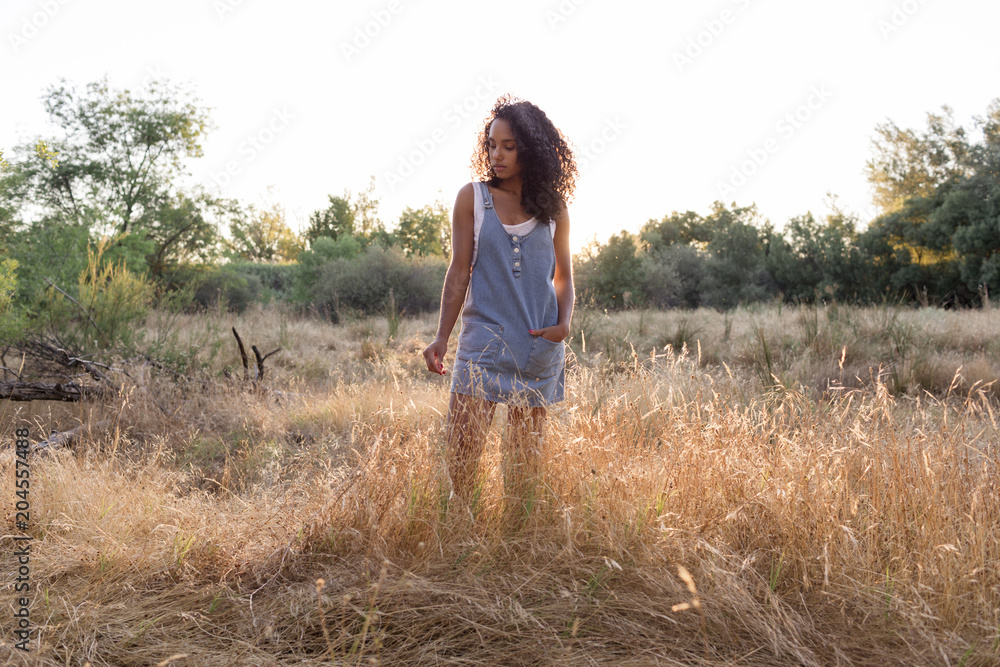 portrait outdoors of a beautiful happy young afro american woman smiling at sunset. Yellow background. Lifestyle in nature. Casual jean dress clothing