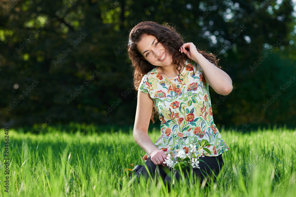 beautiful girl sitting on a glade in the park, bright sun and shadows on the grass beautiful girl sitting on a glade in the park, bright sun and shadows on the grass