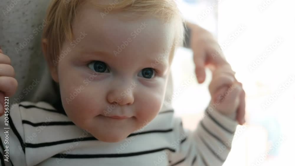 cute excited blonde baby boy sitting at home holding mother's hands cheerful smiling glad happy infant beautiful shy smile lovely blue eyes little caucasian male person portrait child care maternity