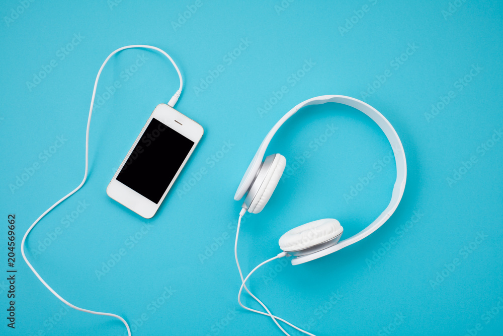 Top view of white earphones with smartphone on blue background. Online music concept - obrazy, fototapety, plakaty 