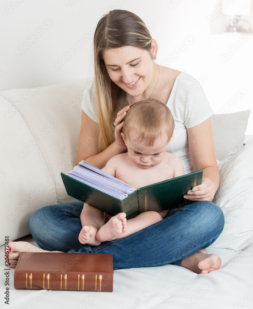 Cute baby boy sitting on mother lap and watching pictures in big old book