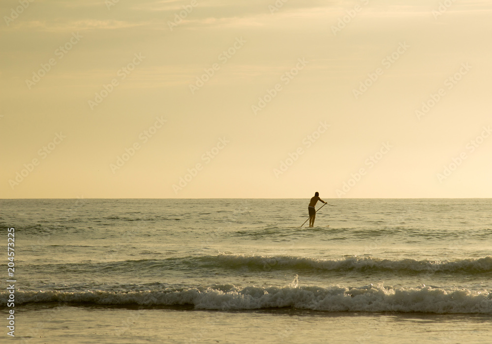 man in the ocean standing on paddle board during sunset