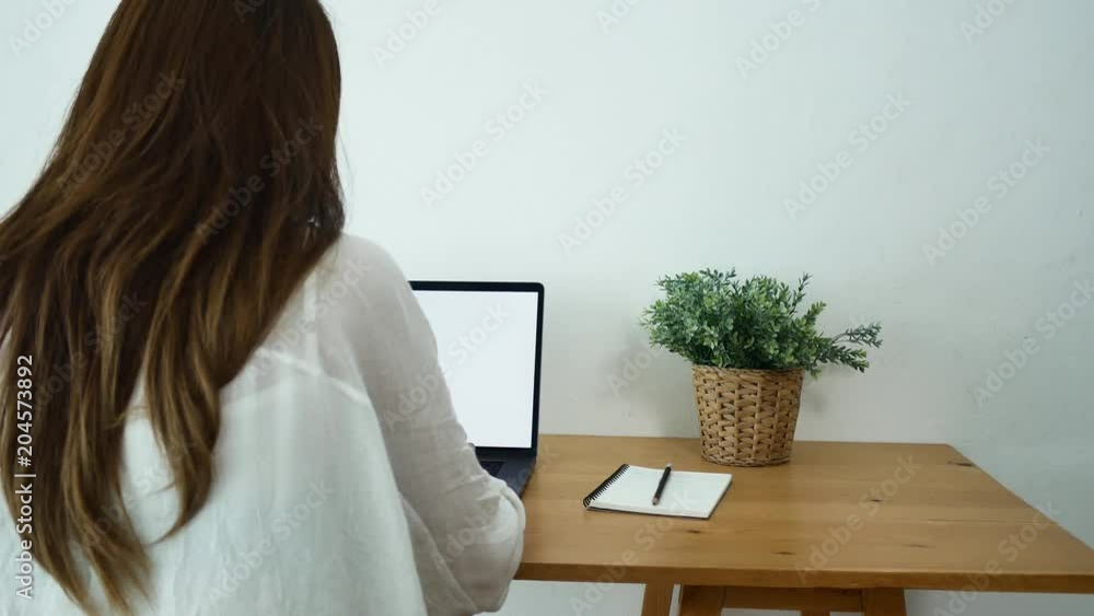Beautiful young smiling asian woman working on laptop while sitting in a living room at home. Asian business woman working in her home office. Enjoying time at home. Beautiful young smiling asian woman working on laptop while sitting in a living room at home. Asian business woman working in her home office. Enjoying time at home.