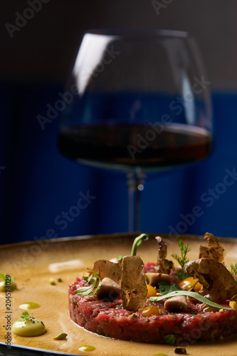 Fototapeta Naklejka Na Ścianę i Meble -  Chopped baked meat cutlet and egg yolk on plate and glass of dry red wine . Luxurious tasty meat dish with various spices and vegetables, close-up