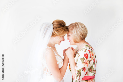 Wedding morning of the bride. Mother of the bride blesses the bride for a happy family life. Mom and her daughter joined hands. In the background a bright wall