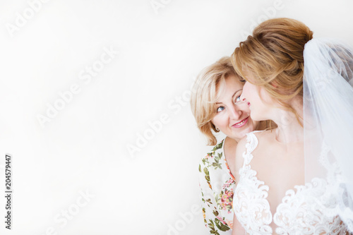 Mom congratulates the brides with a marriage and hugs. woman welcomes. Mom hugs her daughter. In the background a light wall 