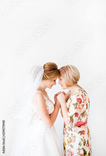 Wedding morning of the bride. Mother of the bride blesses the bride for a happy family life. Mom and her daughter joined hands. In the background a bright wall