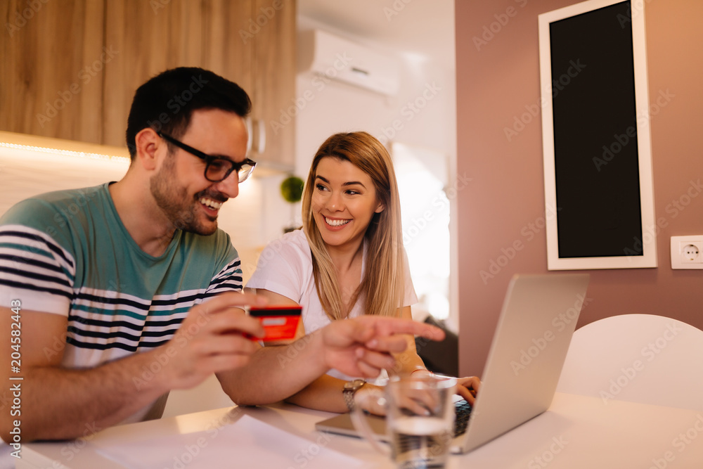 Smiling young couple shopping online while sitting at home Smiling young couple shopping online while sitting at home