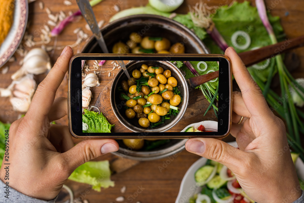 Phone photography of food. Woman hands take photo of lunch with smartphone for social media. Cooked new potatoes in pot with onion and olive oil or butter. Raw vegan vegetarian healthy dinner Phone photography of food. Woman hands take photo of lunch with smartphone for social media. Cooked new potatoes in pot with onion and olive oil or butter. Raw vegan vegetarian healthy dinner