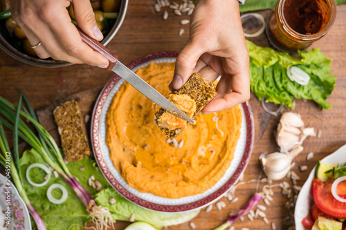 Woman hands spreads hummus on raw bread. Traditional Israel food - dip or spread with chickpea, tahini. . Served with vegetables Greek salad and greens. Raw vegan vegetarian healthy food