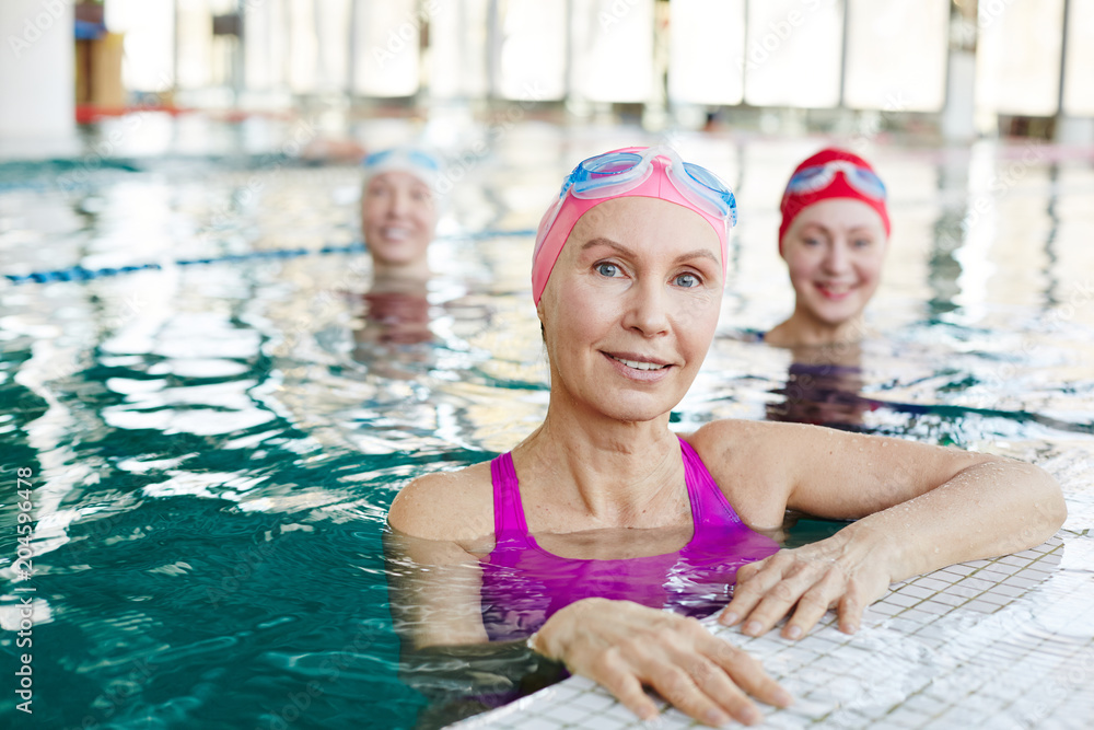 Healthy mature sportswoman and her friends in swimwear spending time in swimming-pool