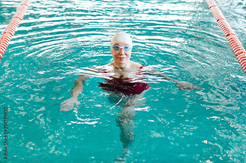 Active female swimmer in swimwear training in water at leisure in sports center