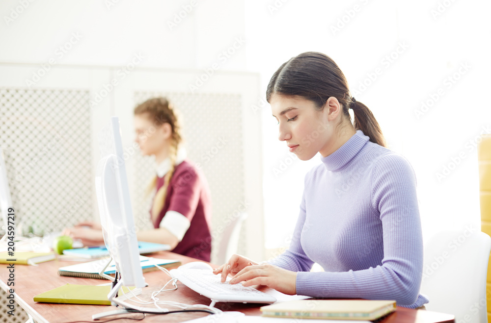Serious young programmer typing on computer keypad while sitting in front of monitor in classroom Serious young programmer typing on computer keypad while sitting in front of monitor in classroom