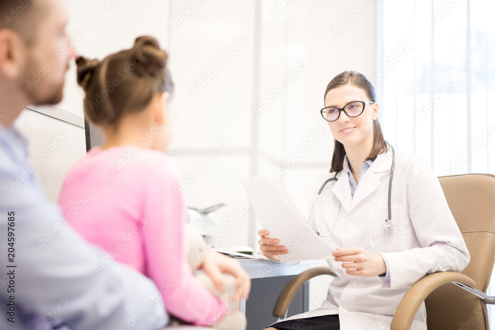 Young smiling clinician with paper talking to father of her little patient during medical appointment Young smiling clinician with paper talking to father of her little patient during medical appointment