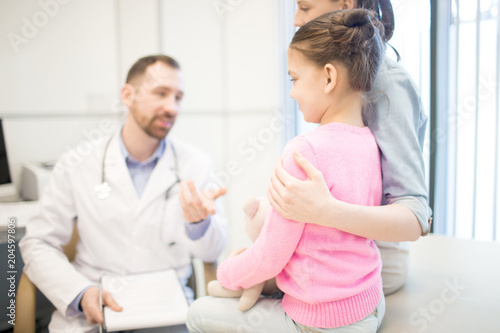 Young female embracing her daughter while listening to clinician at medical appointment