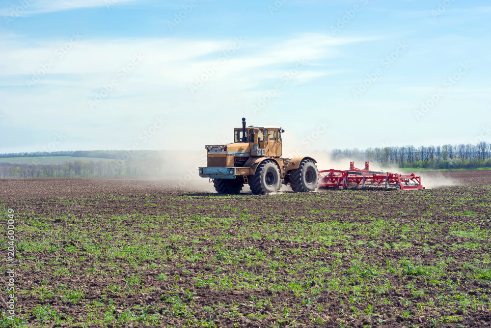 an old tractor is dragging a modern aggregate for tillage leveling the field surface and interrupting weeds an old tractor is dragging a modern aggregate for tillage leveling the field surface and interrupting weeds