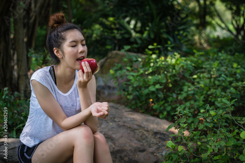 A woman sitting on the stone at park and eating red an apple