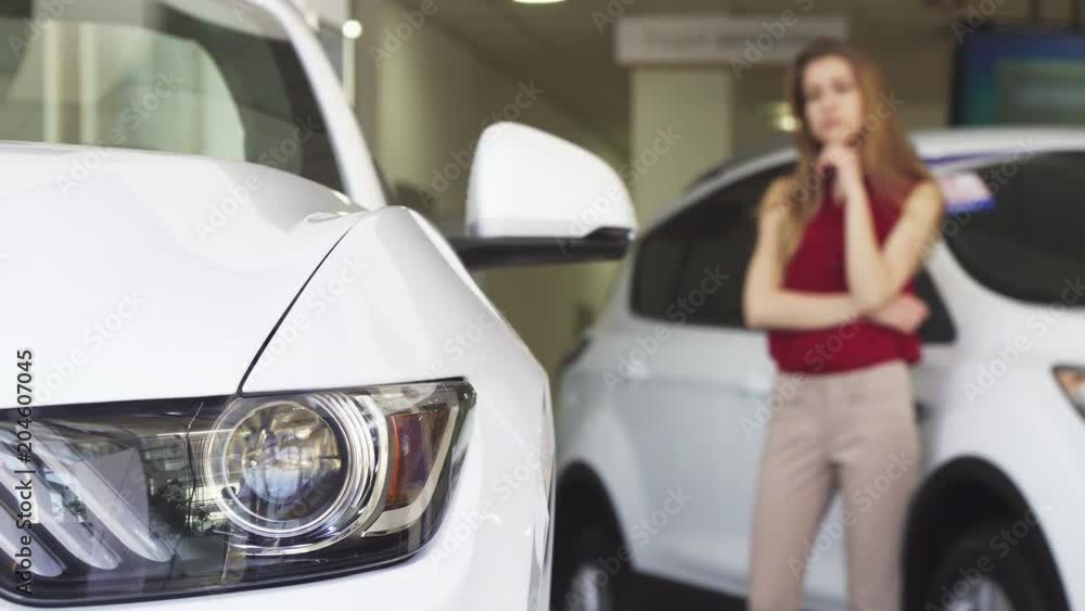 Selective focus on car light female driver shopping for a new vehicle at the dealeship salon copy space. Consumerism, transportation concept. Woman choosing new auto. Selective focus on car light female driver shopping for a new vehicle at the dealeship salon copy space. Consumerism, transportation concept. Woman choosing new auto.