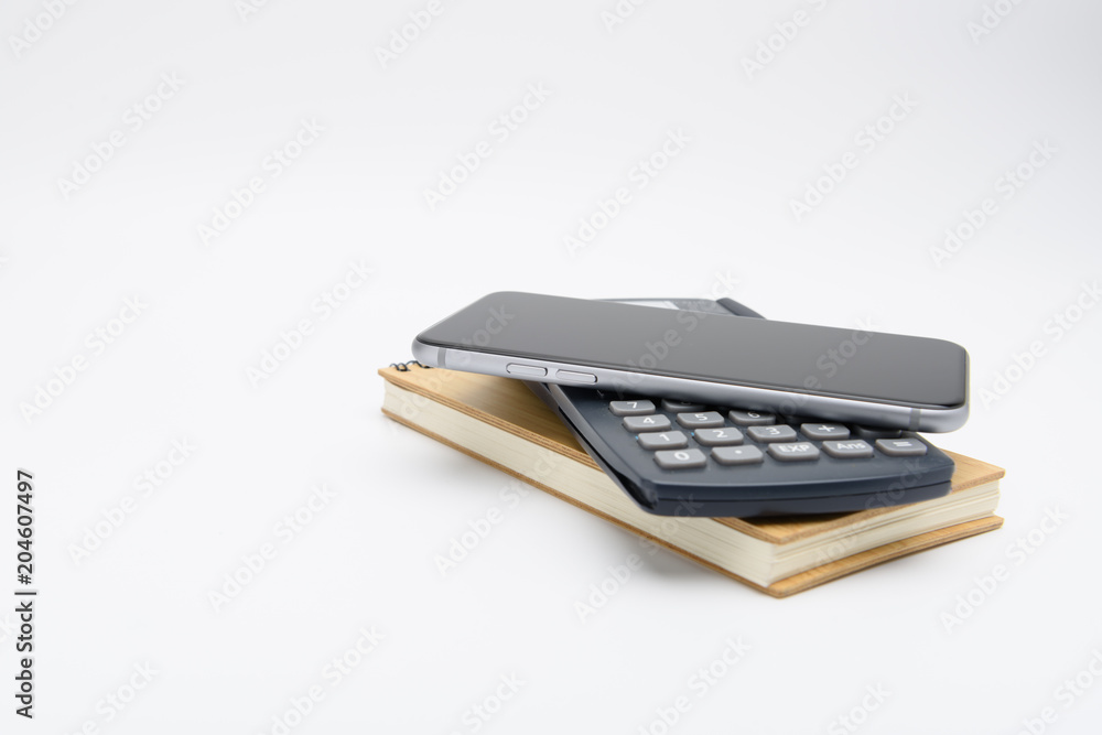 Smart phone, calculator and notepad stacked together on white background.