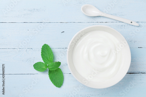 Greek yogurt in bowl decorated mint leaf on blue rustic table top view.