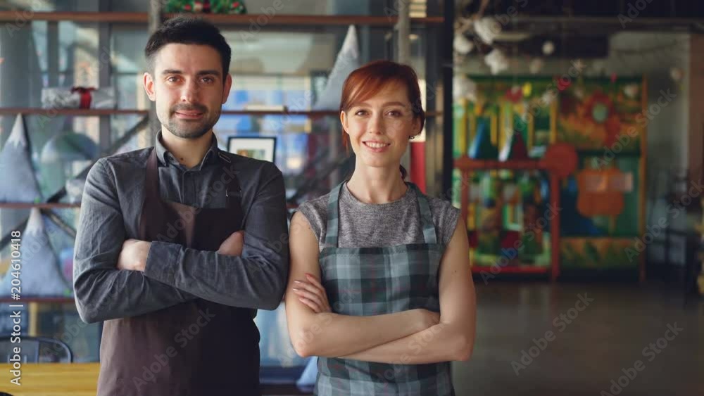 Portrait of two proud small business owners standing inside new spacious cafe and smiling. Successful business start-up, happy people and food service concept. Portrait of two proud small business owners standing inside new spacious cafe and smiling. Successful business start-up, happy people and food service concept.