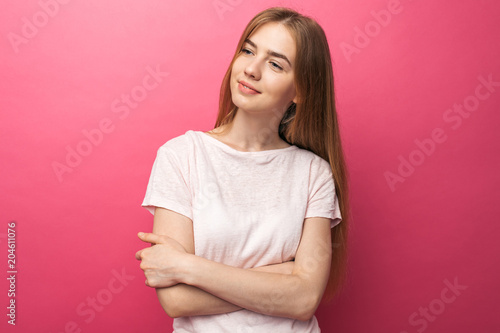 Portrait of a beautiful young girl standing on pink background looking at the camera, smiles and is happy