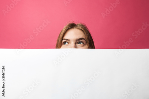 Bilde på lerret Beautiful young girl peeking out from behind white paper wall, on rose backgroun