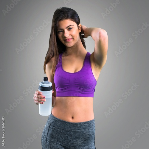 Young sport girl with a bottle on grey background