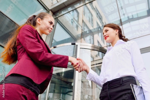Handshake of two young girls against the background of a multi-storey office building. Make a deal. Friendly relations. Office staff