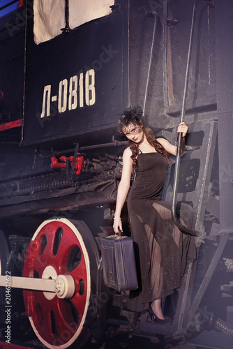 A woman in a vintage black dress with a large suitcase in her hand on an old train. Portrait of a fashionable woman in retro style.