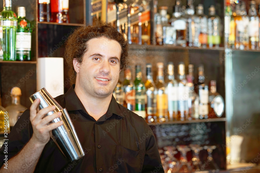 Professional bartender man holding in hands a shaker with a fresh delicious cocktail. Bartender shaking a cocktail shaker as she stands behind the bar mixing a drink for a client. Toning Professional bartender man holding in hands a shaker with a fresh delicious cocktail. Bartender shaking a cocktail shaker as she stands behind the bar mixing a drink for a client. Toning