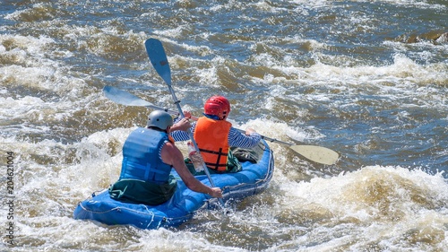 Rafting, kayaking. Two sportsmen in sports equipment are sailing on a rubber inflatable boat in a boiling water stream. Teamwork. Water splashes close-up. Extreme sport. photo