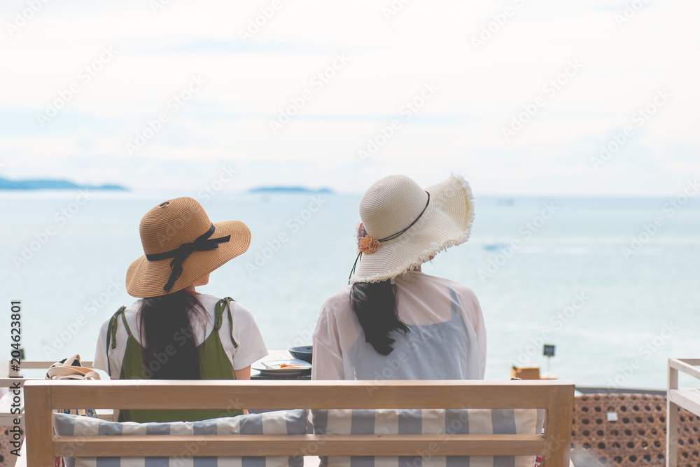 Two women sitting facing the sea, travel concept