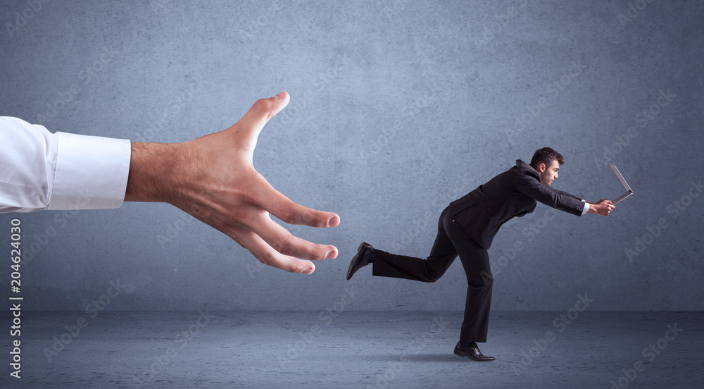 Young miniature businessman running from a big hand with blueish grey background Young miniature businessman running from a big hand with blueish grey background