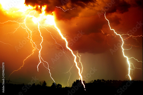Lightning strike on the dark cloudy sky. Orange, yellow and red toned image
