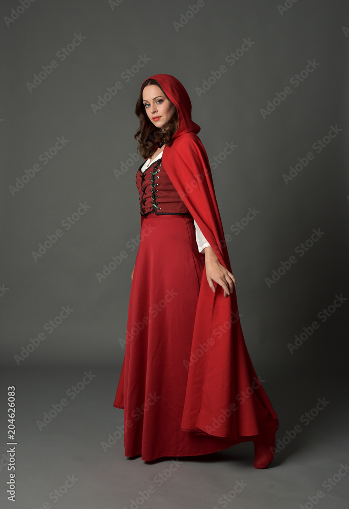 full length portrait of woman wearing red fantasy costume with cloak, standing pose on grey studio background. full length portrait of woman wearing red fantasy costume with cloak, standing pose on grey studio background.