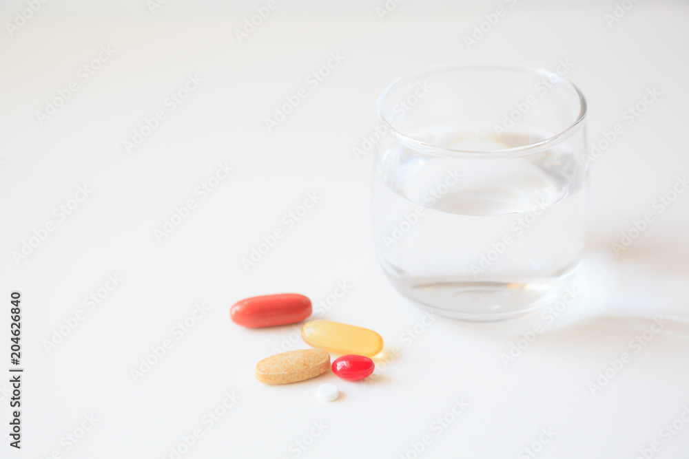 selective focus on a glass of water and medicine pills on white table background selective focus on a glass of water and medicine pills on white table background