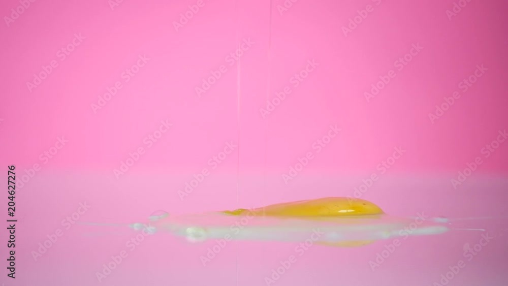 A broken egg falls on the table on the pink background A broken egg falls on the table on the pink background