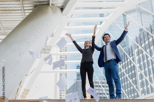 Asian businessman and businesswoman throwing paper in the air and raising up two hands to cheerful and celebrated for successful in career and mission. concept of winner and competition. photo