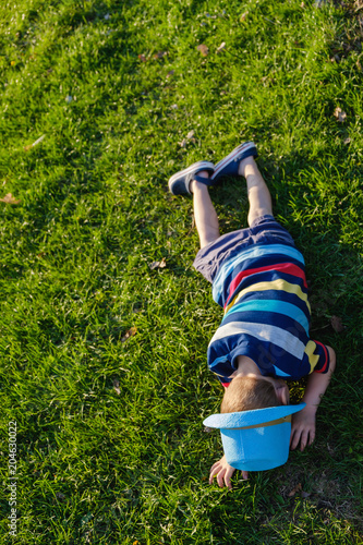 Handsome little boy lying on grass. Little dreamer lies in meadow with hat. Child in nature outside city. Carefree vacation